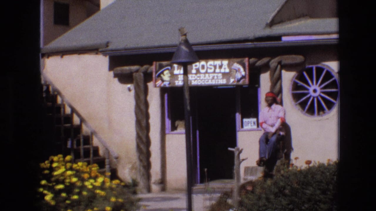 Closer storefront view with La Posta sign, open sign, wagon-wheel window, and seated man outside.