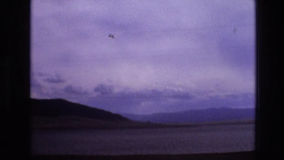 1973 New Mexico 8mm frame showing a calm lake, silhouetted shoreline hills, and distant mountains under a purple-blue evening sky.