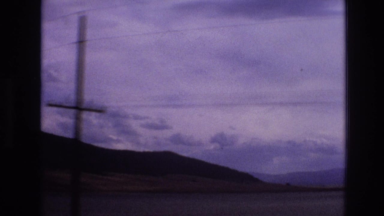 1973 New Mexico roadside frame with a utility pole and power lines crossing a silhouetted mountain ridge under a cloudy purple-blue sky.