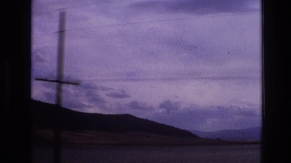 1973 New Mexico roadside frame with a utility pole and power lines crossing a silhouetted mountain ridge under a cloudy purple-blue sky.