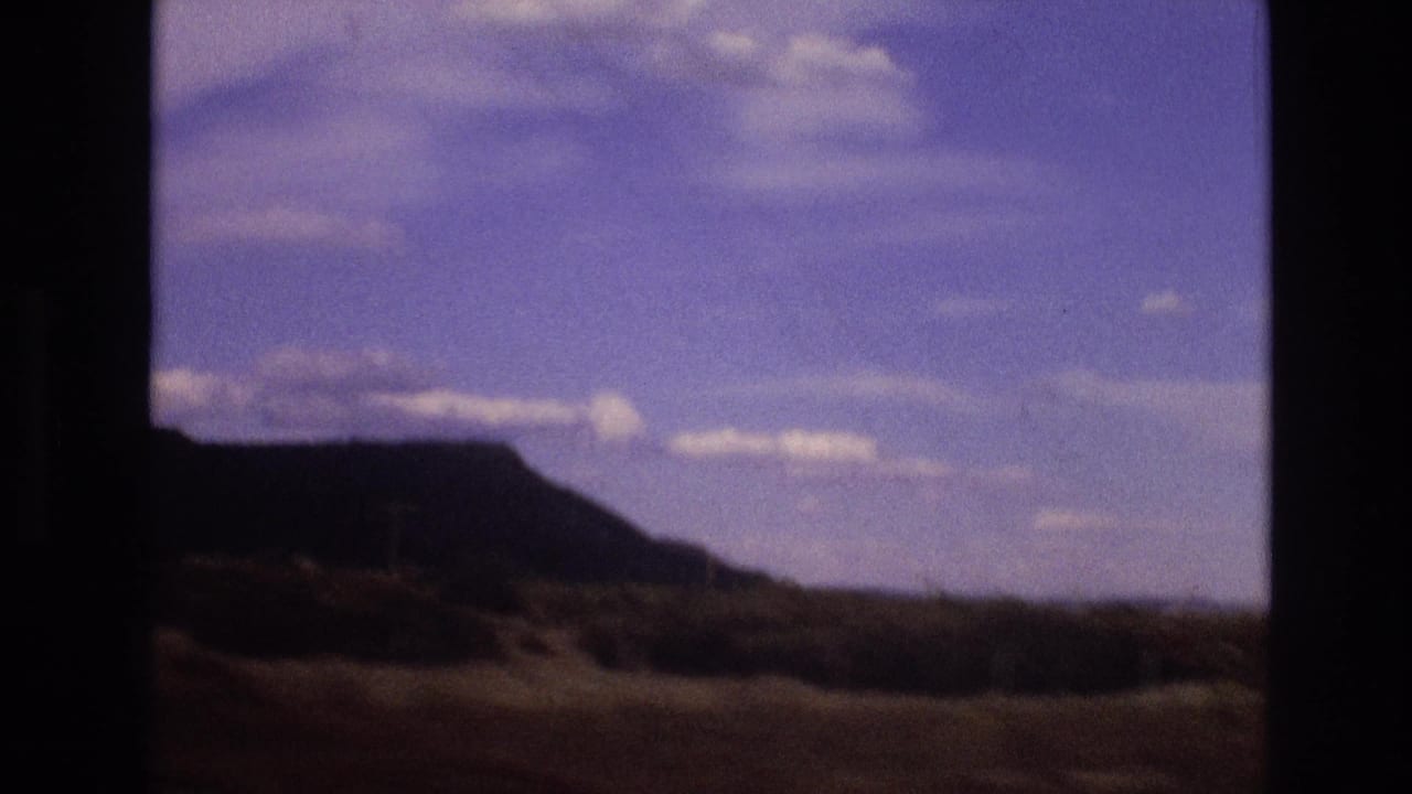 Rocky hill silhouette beneath a blue clouded sky, seen through a dark window frame.