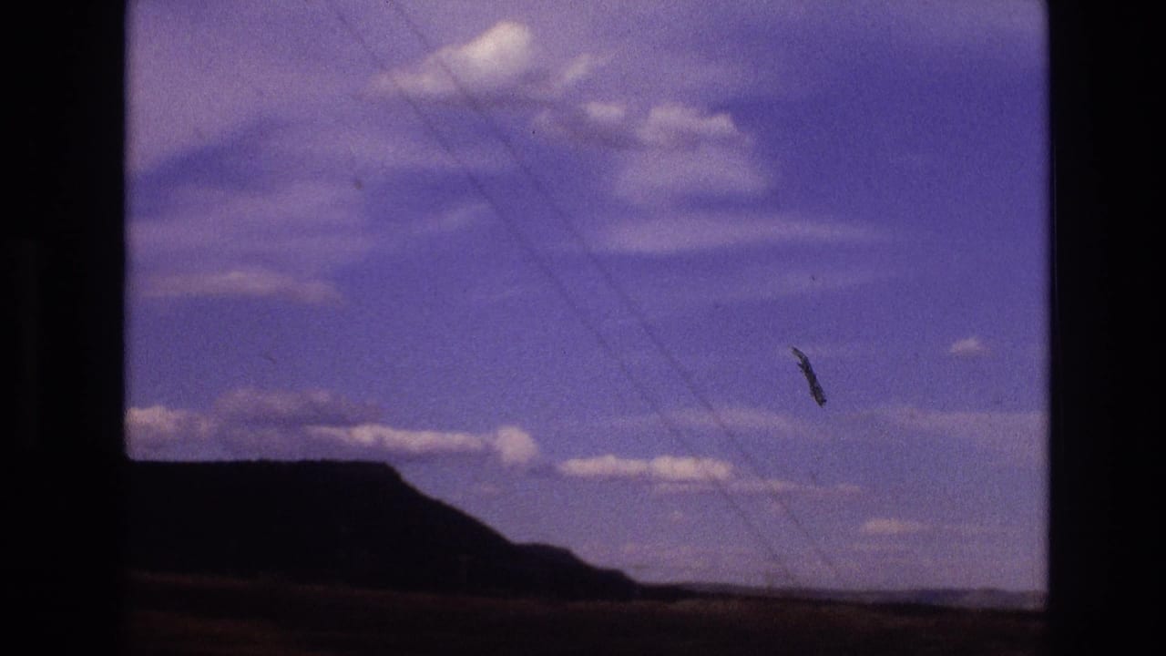 1973 New Mexico 8mm road-view frame showing a dark desert hill, open sky, scattered white clouds, faint power lines, and black film-scan borders.