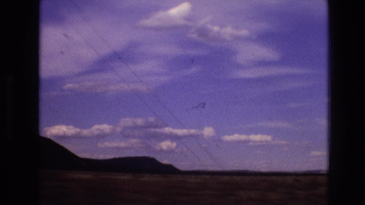 1973 New Mexico 8mm frame showing a distant low hill line under a purple-shifted cloudy sky, with dark contact-sheet borders and soft focus.