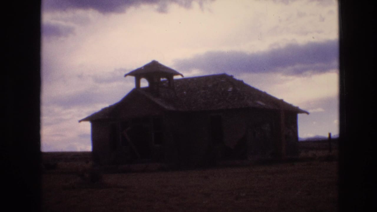 Abandoned rural building with a broken roof and dark openings on flat land.