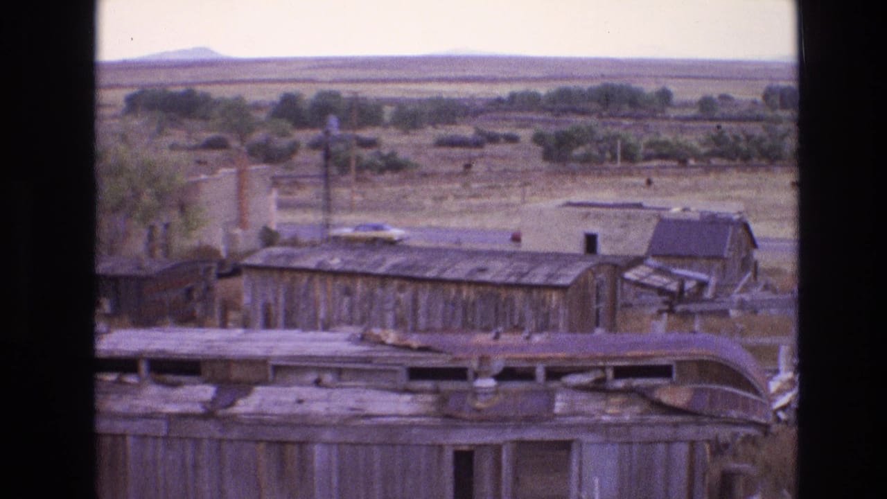 Abandoned station structures with a parked car and broad plains in the distance.