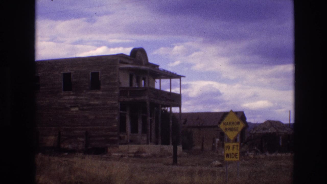 1973 New Mexico 8mm frame showing a weathered wooden roadside building with balcony framing and a yellow narrow bridge sign in dry grass.