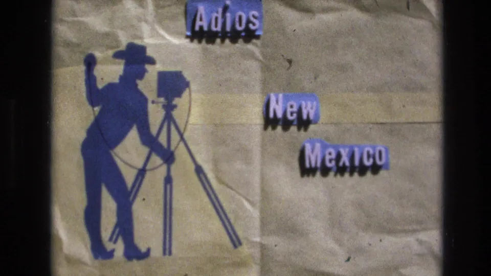 1973 home-movie title card reading "Adios New Mexico" with a blue silhouette of a person operating a film camera against a wrinkled paper-like background.