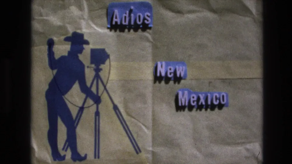 1973 New Mexico 8mm frame showing the same handmade farewell card, with the blue cowboy photographer silhouette at left and "Adios New Mexico" lettering at right.