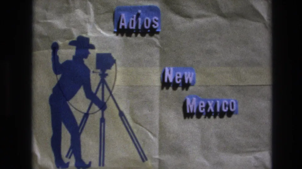 1973 New Mexico 8mm home-movie title card showing blue cut-out text reading Adios New Mexico beside a cowboy photographer silhouette with a tripod camera.