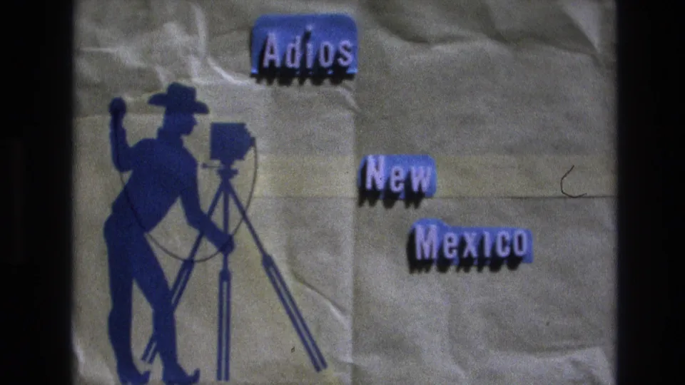 1973 New Mexico 8mm frame showing a handmade farewell title card with blue lettering, a cowboy photographer silhouette, a tripod camera, and visible film texture.