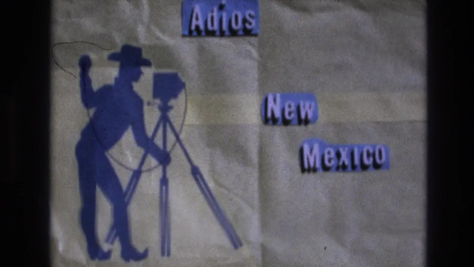 1973 New Mexico 8mm frame of a handmade farewell title card with a cowboy in profile operating a tripod camera and purple “Adios New Mexico” lettering.