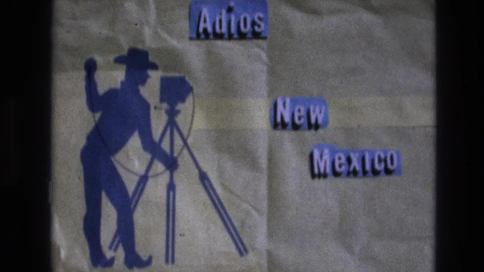 1973 8mm New Mexico title-card frame showing a blue cowboy figure, a camera on a tripod, and separated purple cutout words reading “Adios,” “New,” and “Mexico.”