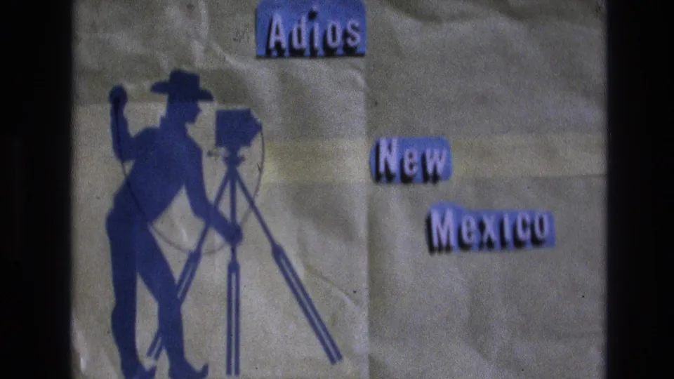 Soft 8mm frame of the 1973 New Mexico farewell card, showing blue Adios and New Mexico lettering, a cowboy photographer silhouette, and crinkled backing paper.