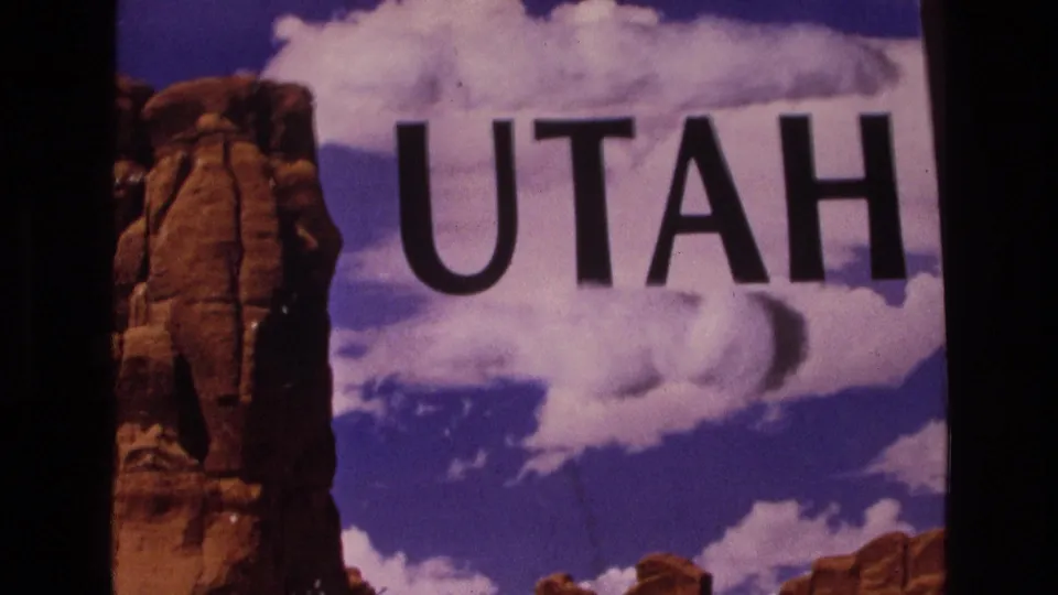 Final visible 1973 Utah title-card frame with black UTAH lettering, red rock formations, white clouds, and dark scan borders from the 8mm source.
