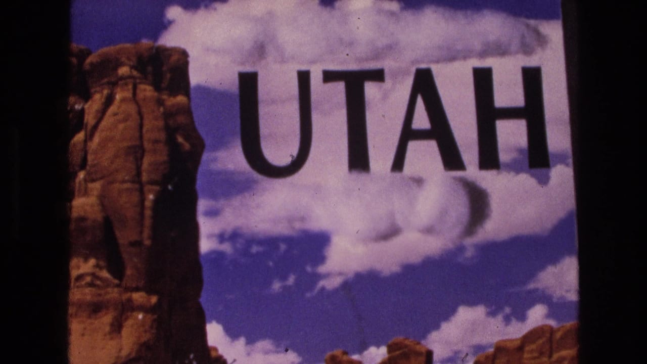 1973 Utah travelogue title card showing large black UTAH text over red rock formations and a bright clouded sky on 8mm film.