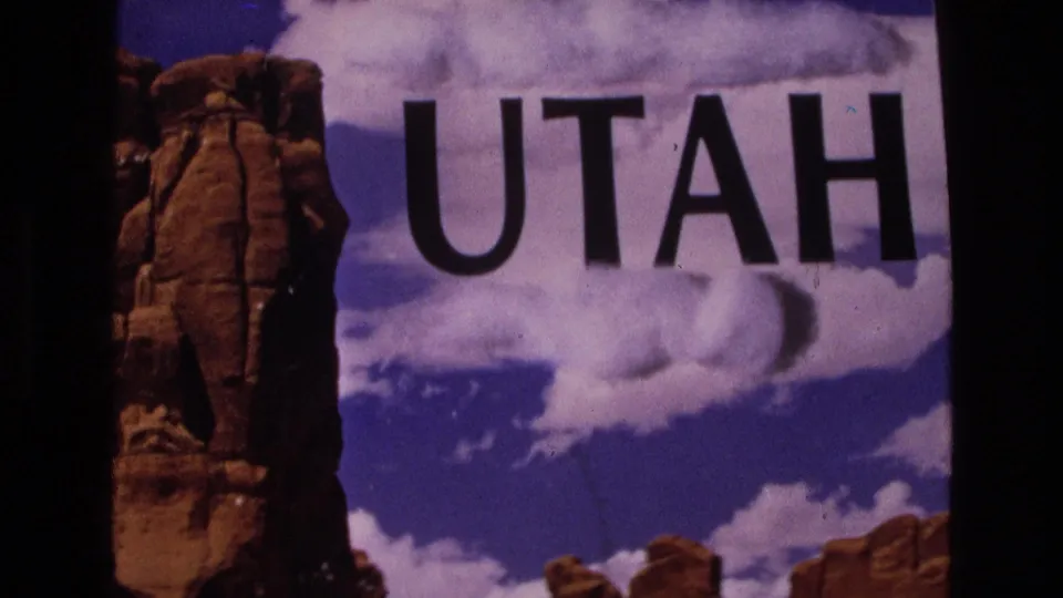 1973 home-movie Utah title card with black UTAH text across a clouded sky and red desert rock formations.