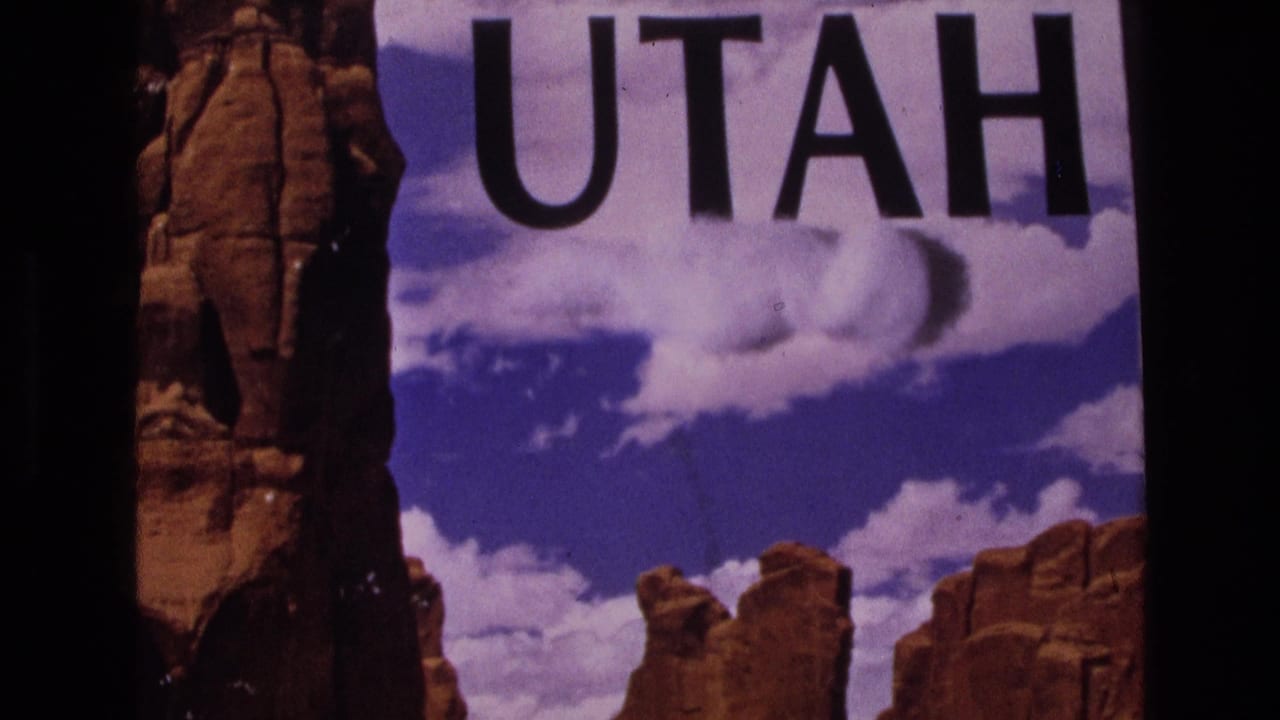 Large UTAH lettering above red sandstone formations and blue sky within a film frame.