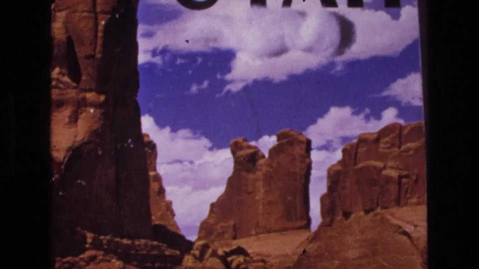 1973 8mm Utah landscape frame showing red sandstone cliffs under a bright sky, with cropped title lettering at the upper edge.