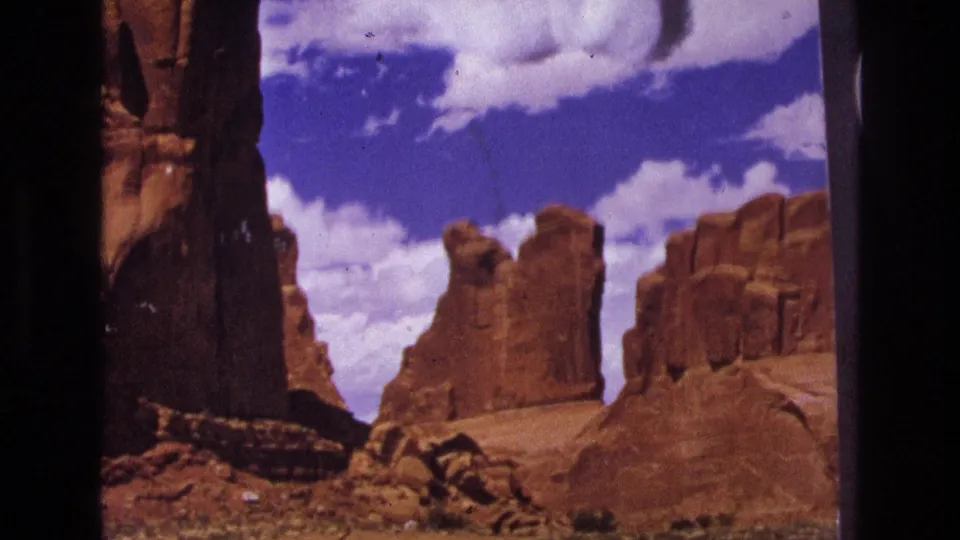 1973 8mm Utah travel frame showing red sandstone formations and open blue sky, with visible film-frame borders and archival grain.