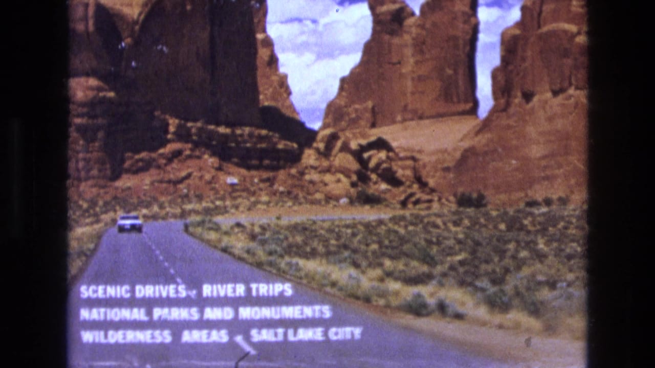 Road and white car beneath red rock formations with readable scenic-drive text.