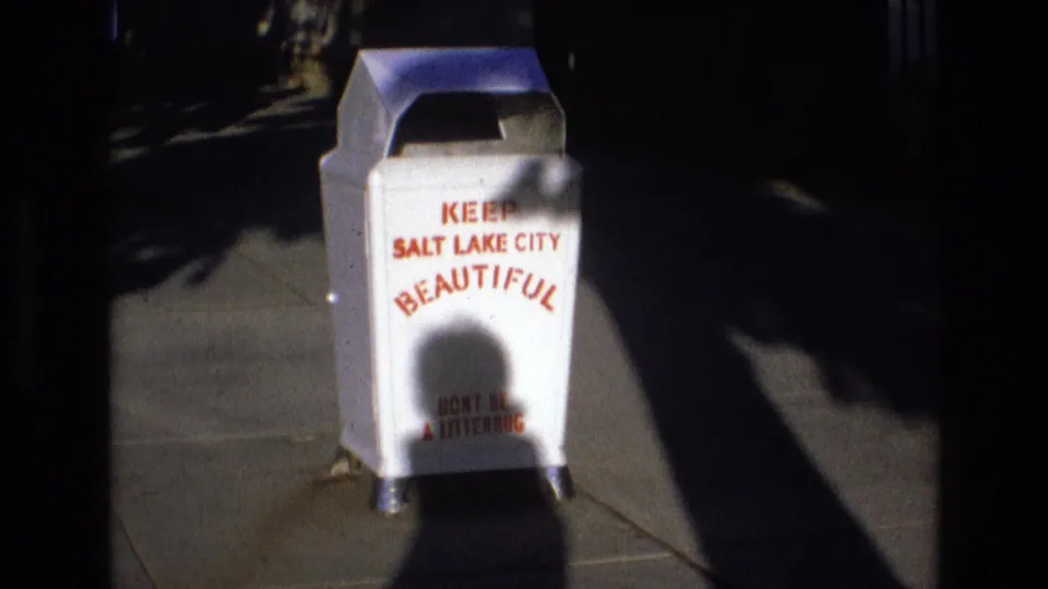 1973 Salt Lake City 8mm frame with the same white public trash can and red anti-litter text, partly softened by home-movie focus and exposure.