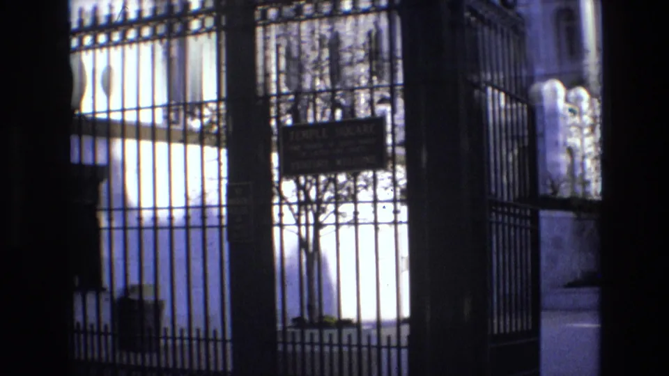 1973 Salt Lake City frame looking through black iron gates toward a Temple Square sign, a tree, stonework, and background buildings.
