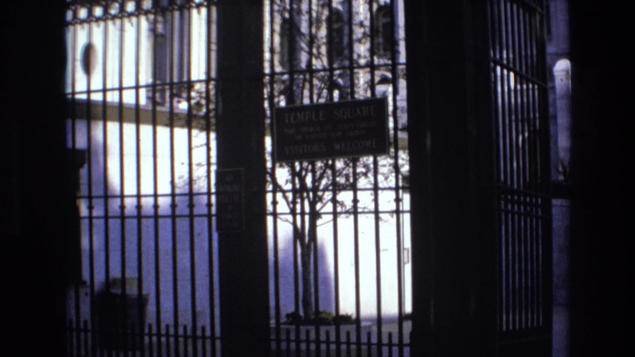 1973 Salt Lake City home-movie frame looking through a wrought iron gate toward a Temple Square visitors welcome sign and smaller no smoking notice.