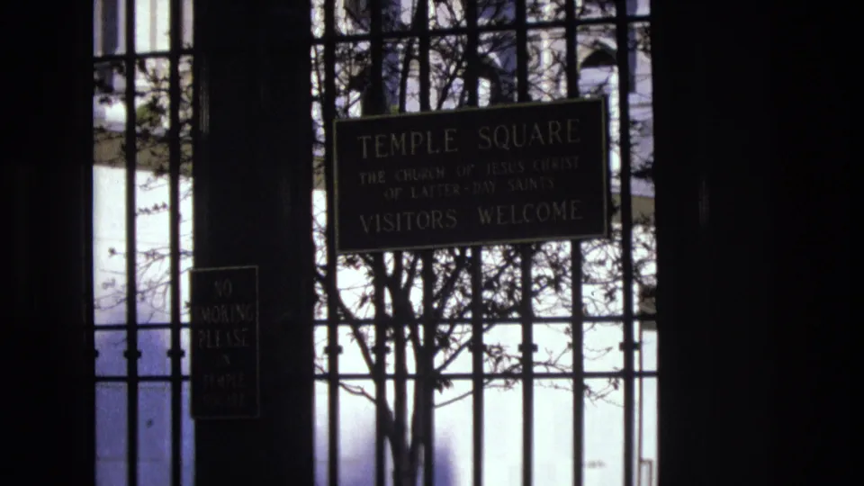 1973 Salt Lake City home-movie frame showing the Temple Square visitors welcome sign, a no smoking notice, and bare branches behind the iron gate.