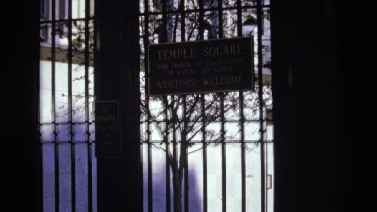 Temple Square gate seen through dark vertical bars with a welcome sign and trees beyond.