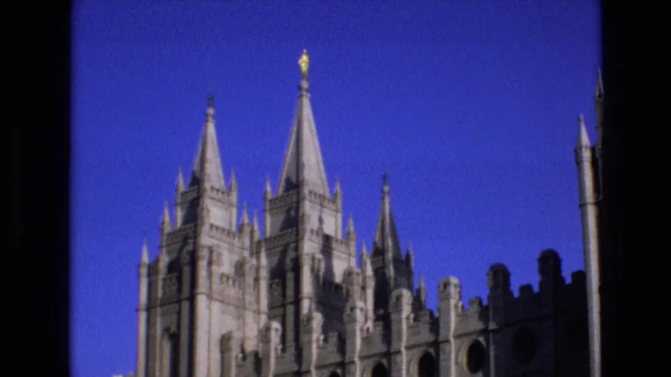 1973 Salt Lake City frame showing the Salt Lake Temple with Gothic spires, pale stonework, and a golden statue visible against a deep blue sky.