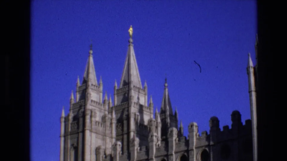 Salt Lake City Temple towers and roofline details in 1973 8mm footage, with the building partially bordered by dark window or structural edges.