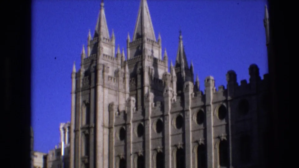 1973 Salt Lake City Temple exterior showing a wider portion of the pale stone facade, pointed spires, circular openings, and a dark vertical border at the frame edge.