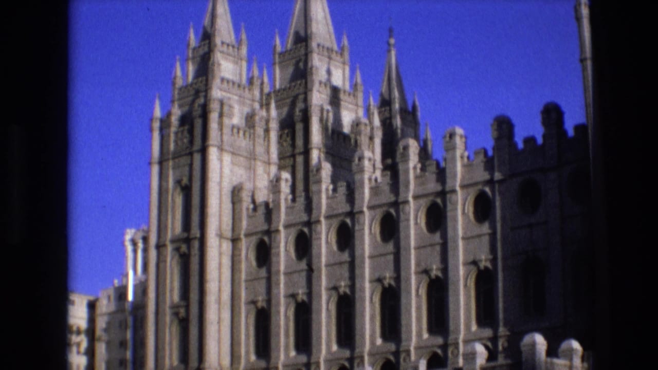 Salt Lake Temple facade seen through dark foreground framing under a blue sky.