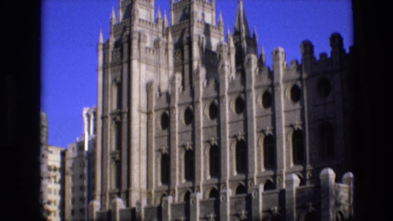 Salt Lake City temple exterior in 1973 home-movie footage, showing vertical spires, decorative stonework, and dark foreground obstruction along the left side.