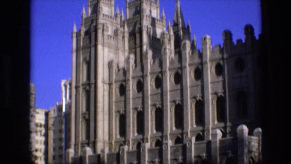 Salt Lake City temple exterior in 1973 home-movie footage, showing vertical spires, decorative stonework, and dark foreground obstruction along the left side.