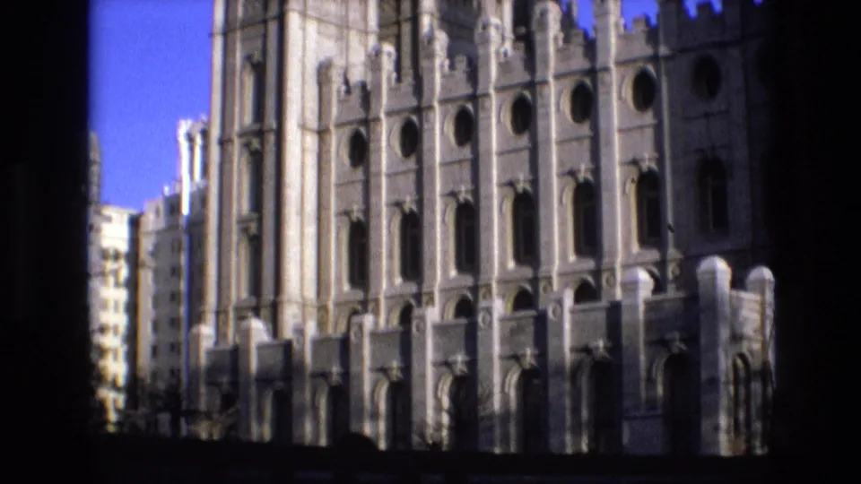 1973 Salt Lake City 8mm frame showing the temple's lower and central facade, dark vertical foreground framing, and a neighboring building at the edge.