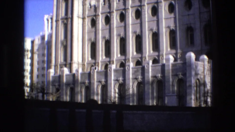 Final 1973 home-movie frame of the Salt Lake Temple exterior, emphasizing the lower facade, repeated arches, round openings, and strong dark foreground border.