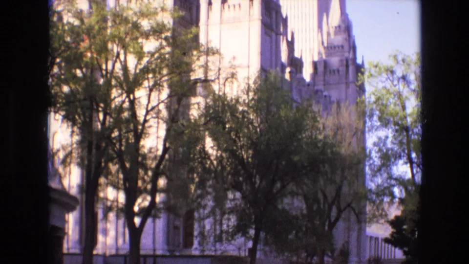 1973 Salt Lake City 8mm frame with Salt Lake Temple stonework visible through sunlit trees and a darker foreground edge.