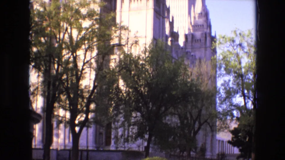 1973 Salt Lake City 8mm frame showing a pale stone urban building behind trees, with dark edge vignetting from the film scan.