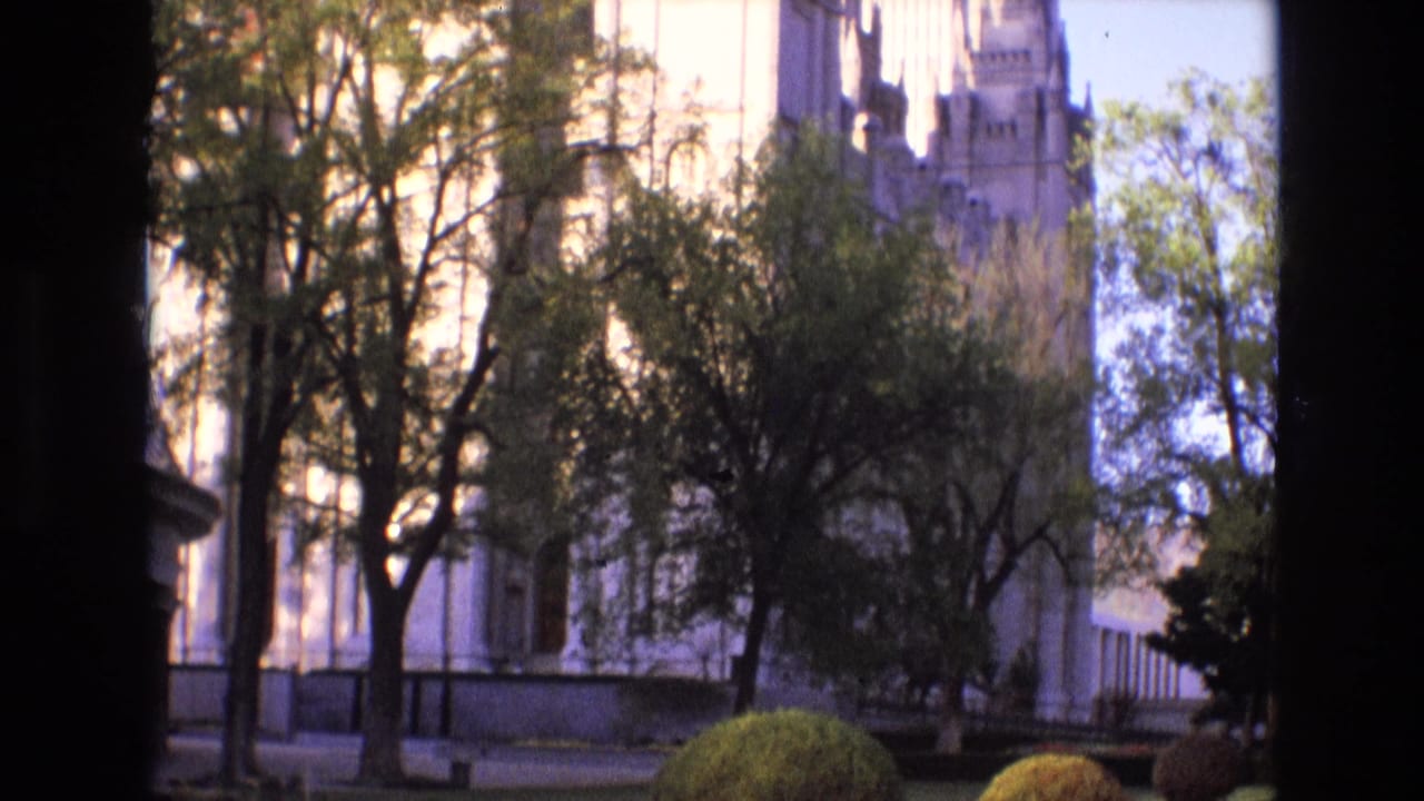 Trees and pale stone building seen through a dark vertical film-frame edge.