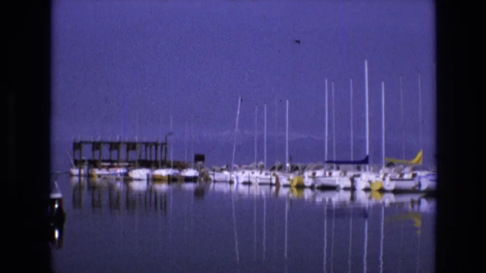 1973 Salt Lake City 8mm marina view with docked sailboats, a small pier, and masts reflected in still water.