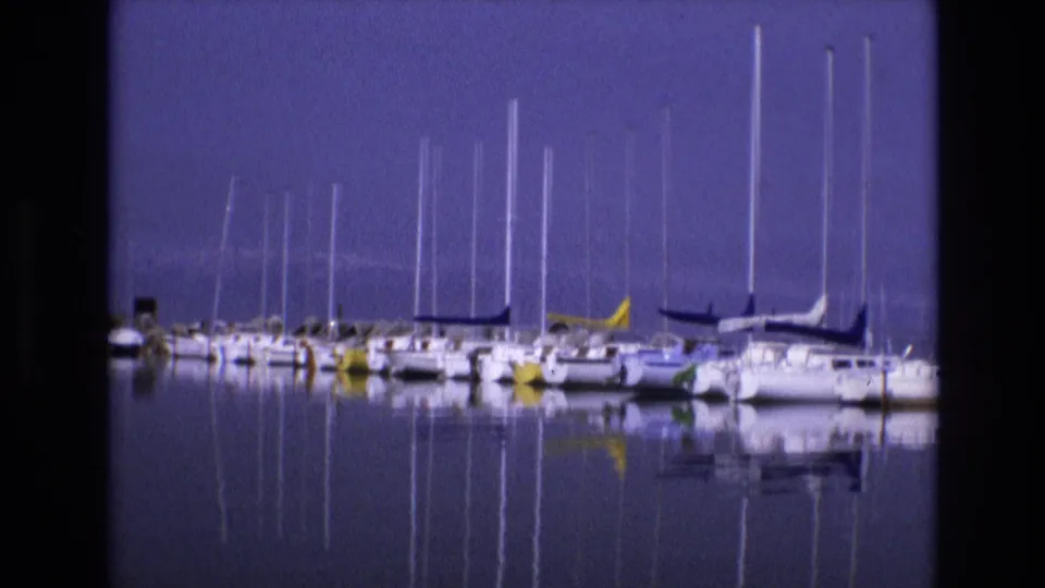 1973 Salt Lake City, Utah 8mm frame with a steady view of white sailboats, dark sail covers, and mirrored masts on calm water.