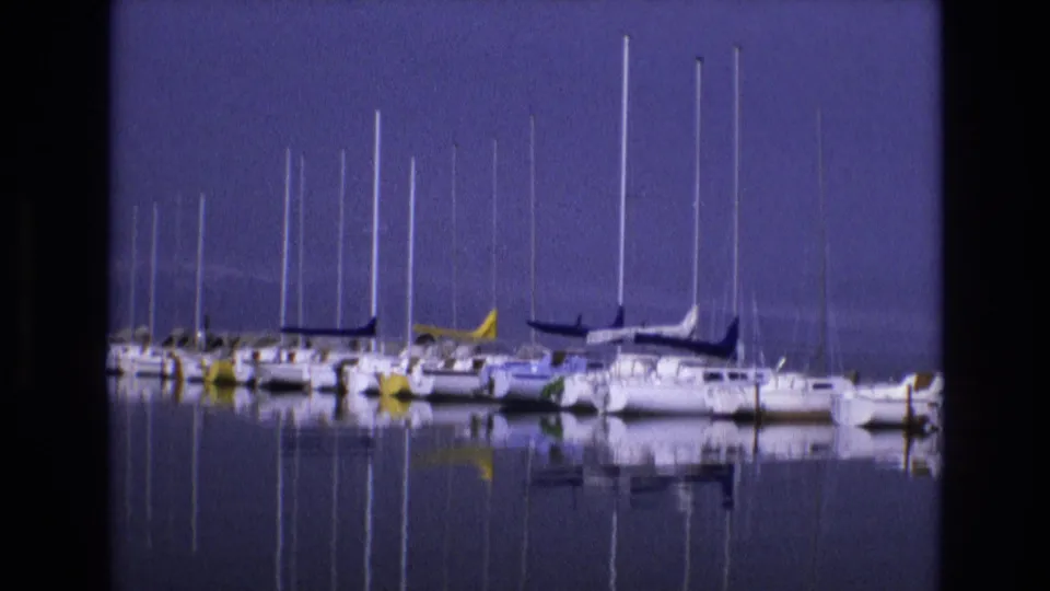 1973 Salt Lake City, Utah 8mm frame showing a closer lineup of sailboats with white hulls, tall masts, and soft reflections across still water.