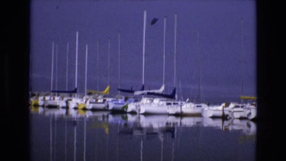 1973 Salt Lake City, Utah 8mm frame showing sailboats moored side by side, their masts and hulls reflected in the smooth marina water.