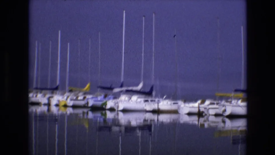 1973 8mm home-movie frame from Salt Lake City, Utah, showing a row of docked sailboats with tall masts and soft reflections on still water.