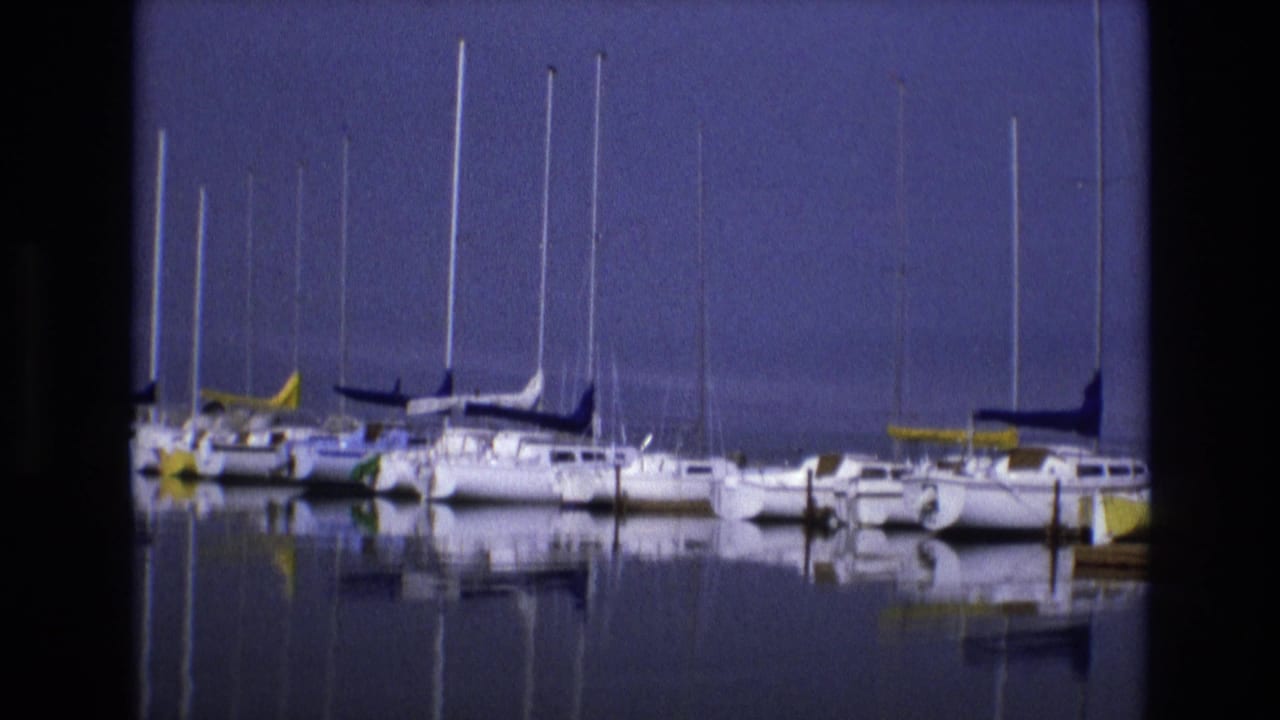 1973 Salt Lake City marina frame with white sailboats, colored sail covers, and vertical mast reflections across calm water.
