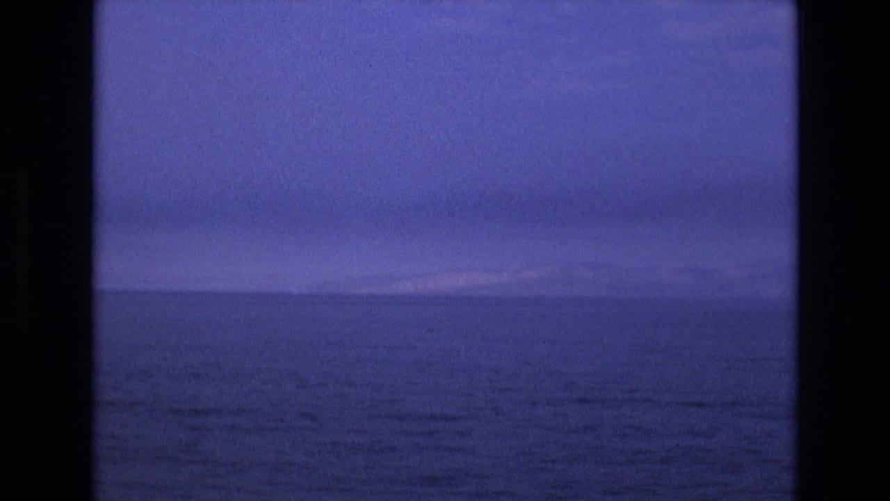 1973 8mm Salt Lake City-area frame with open dark water, a faint distant shoreline or mountain line, and a cool blue twilight sky.
