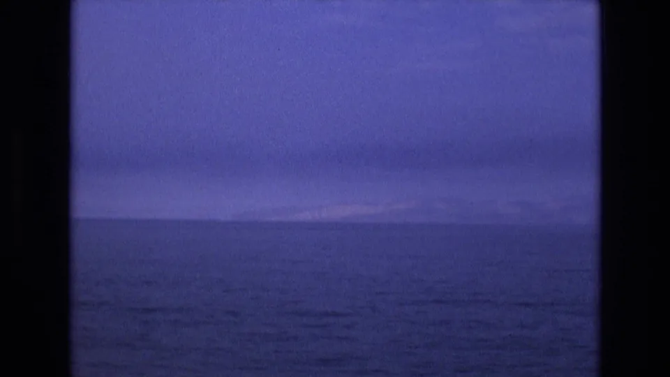 1973 8mm Salt Lake City-area frame with open dark water, a faint distant shoreline or mountain line, and a cool blue twilight sky.