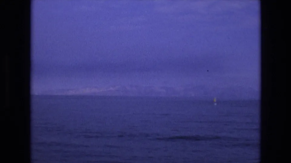 1973 8mm Salt Lake City-area footage showing calm dark water, a low horizon, faint distant land, and a small yellow buoy near the center-right distance.