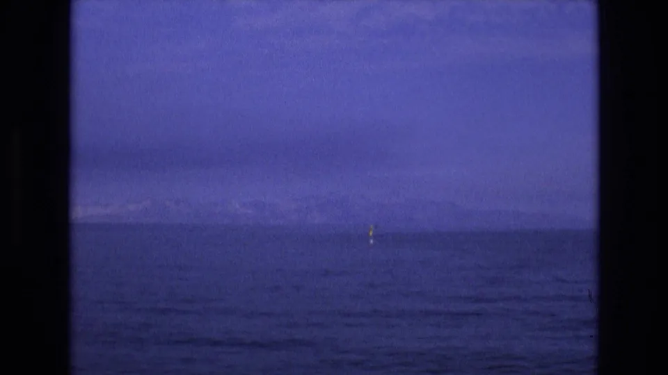 1973 8mm Salt Lake City-area frame with a small yellow buoy against dark rippled water, a faint horizon, and blue-purple twilight sky.